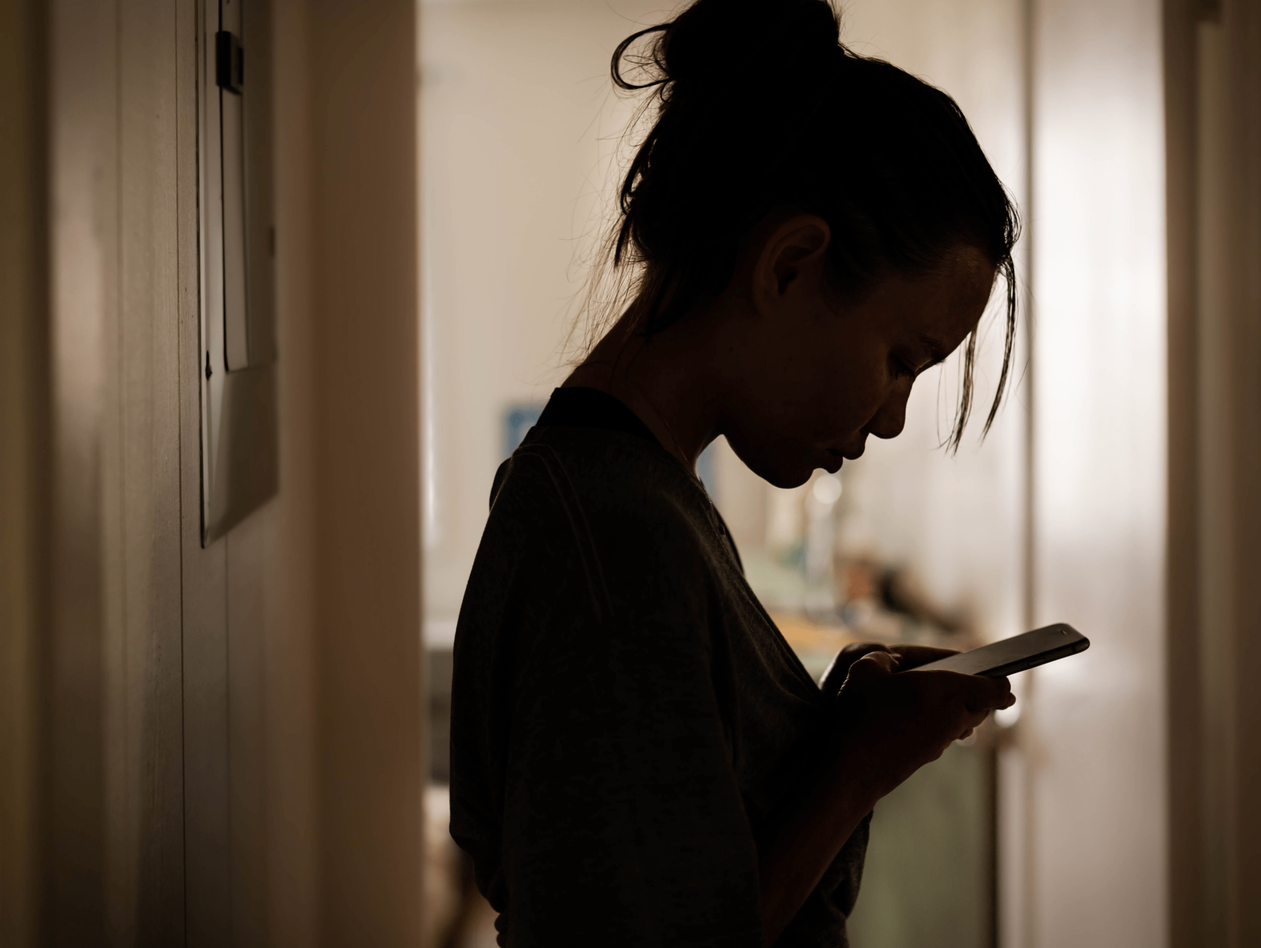 Silhouette of woman alone in dark hallway on phone representing isolation and emotional struggle treated with IV ketamine therapy at Better Health Whole Wellness Center Rittenhouse Square Philadelphia
