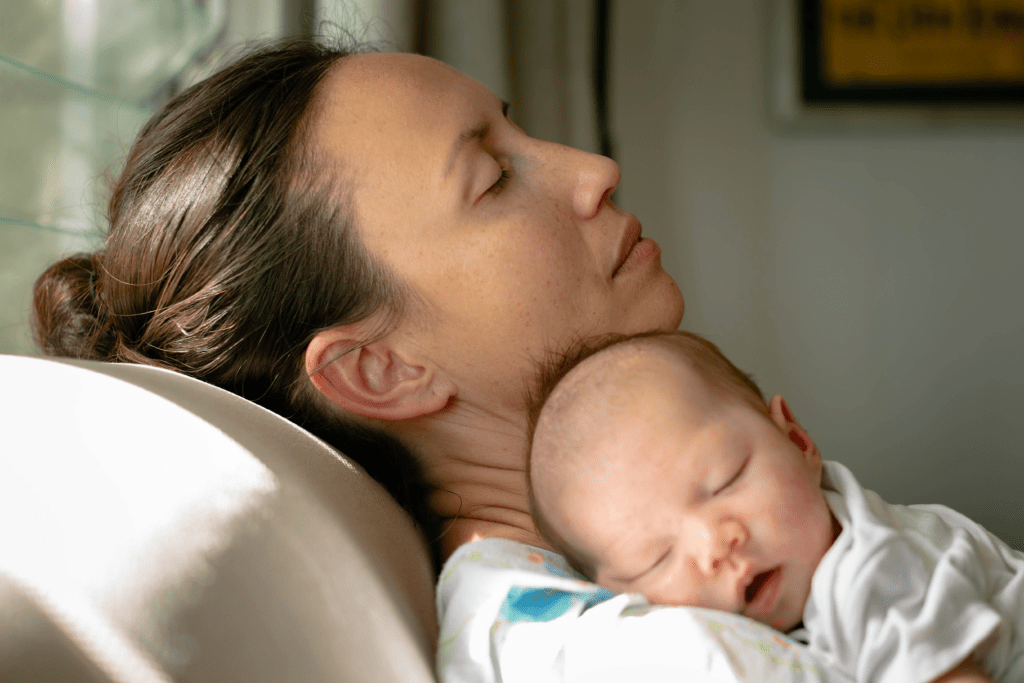 Exhausted new mother resting with sleeping newborn representing postpartum depression and the need for treatment in Philadelphia